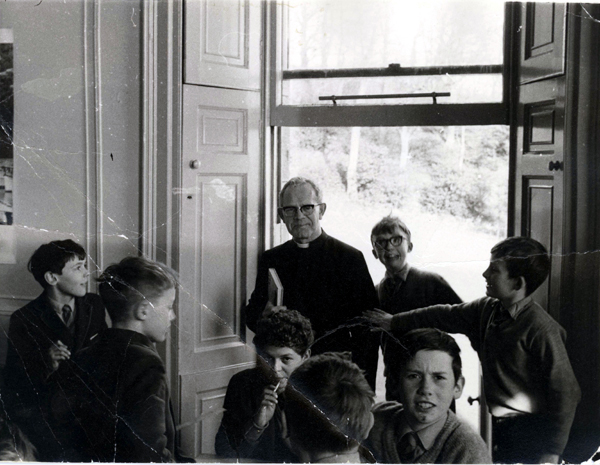ClassRoom3a.jpg - That's Gary in the middle with something in my mouth, a paint brush I  think. Iain Mc? is looking straight in to the camera to the right. I  can't recall any of the others although the boy on the far lefts name  is on the tip of my tongue, is It Aden! The classroom was on the far  > east side of the main building, on the front corner. The window could  open up and let us out onto the lawn. Naldo Forte let us know that he is the boy on the right with his hand out touching the teacher, he also states that it is Richard Eddie standing in in the doorway.  